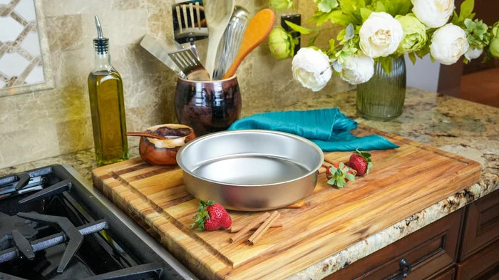 Angled view of 9-inch round cake pan showcasing stainless-steel interior and rolled rim on wooden cutting board on kitchen countertop