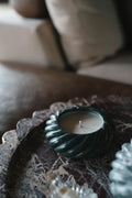 A decorative candle in a green stone spiral holder sits on a marble tray, with blurred cushions in the background.