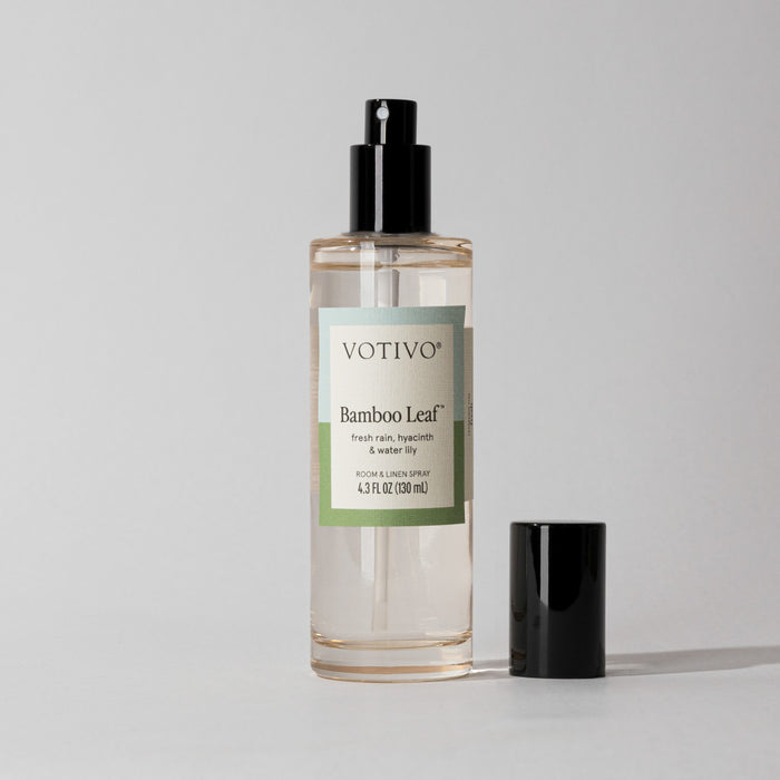 A clear Votivo Bamboo Leaf Room & Linen Spray bottle with a black nozzle and cap beside it rests on a simple background, emphasizing its fresh scent and signature bamboo leaf fragrance.