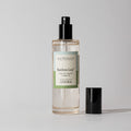 A clear Votivo Bamboo Leaf Room & Linen Spray bottle with a black nozzle and cap beside it rests on a simple background, emphasizing its fresh scent and signature bamboo leaf fragrance.