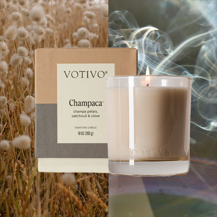 On the left, a Votivo Champaca 10 oz. Signature Candle box set rests in dry grasses, while on the right, a lit Votivo soy blend candle in glass holder emits swirling smoke for an unforgettable fragrance experience.