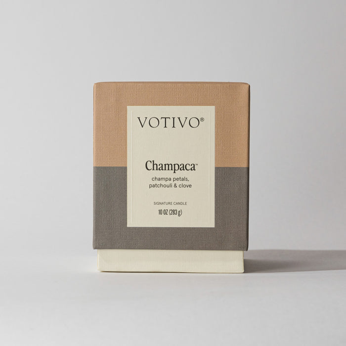 The Votivo Champaca 10 oz. Signature Candle, in a minimalist beige, taupe, and gray box, features notes of champa petals, patchouli & clove for a unique fragrance experience.