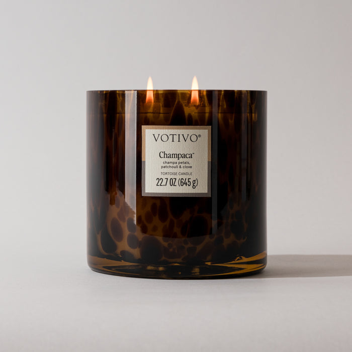 The Votivo Champaca Tortoise Candle is a 22.7 oz (645 g) soy blend candle with two flames in a brown tortoiseshell vessel, shown against a plain light background.