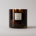 The Votivo Champaca Tortoise Candle is a 22.7 oz (645 g) soy blend candle with two flames in a brown tortoiseshell vessel, shown against a plain light background.