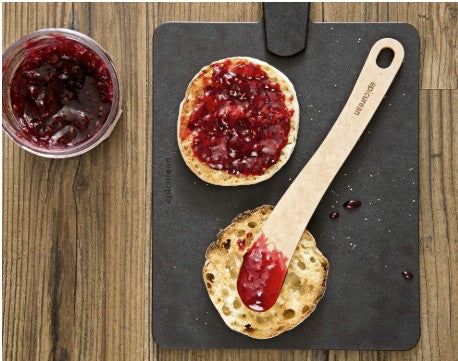 Top view of Epicurean large spoon spatula showing thin curved blade and stamped handle on a slate with muffins and jam