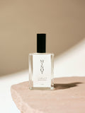 Clear glass bottle of MINOT Cliffwalk room and linen spray with black cap, placed on a textured stone surface, highlighted by soft natural light.