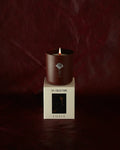A lit LES Collection Ember candle in a dark red vessel sits on a white box labeled "LES Collection Ember." The background is a rich, dark red.