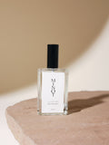 A minimalist glass bottle with a black cap labeled "MINOT Eventide Room & Linen Spray" sits on a stone surface with a soft beige background and shadow.