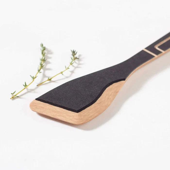 Angled close-up of Frank Lloyd Wright sauté tool showing black Richlite paddle and natural wood handle on white background