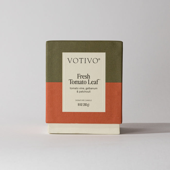 The Votivo Fresh Tomato Leaf 10 oz. Signature Candle features scent notes of tomato vine, galbanum, and patchouli in a soy blend wax, boxed in olive green, rust orange, and cream color blocks.