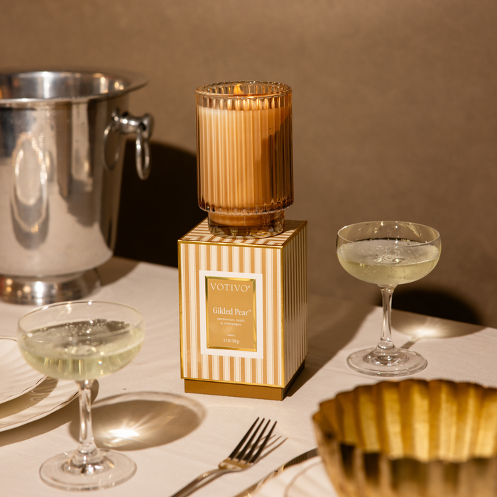 A Gilded Pear Candle with Box sitting on a restaurant table with ice bucket and champage