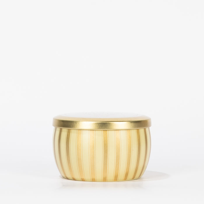 The Votivo Gilded Pear Holiday Tin Candle is a small, round, gold-colored tin with vertical stripes and a matching lid, filled with soy blend wax in a fragrant Gilded Pear scent, displayed against a plain white background.