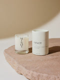 A small soy candle in a glass holder labeled "MINOT" sits on a stone surface next to a cylindrical white cardboard box with text describing the Haven scent as a blend of black currant, jasmine, and vanilla.