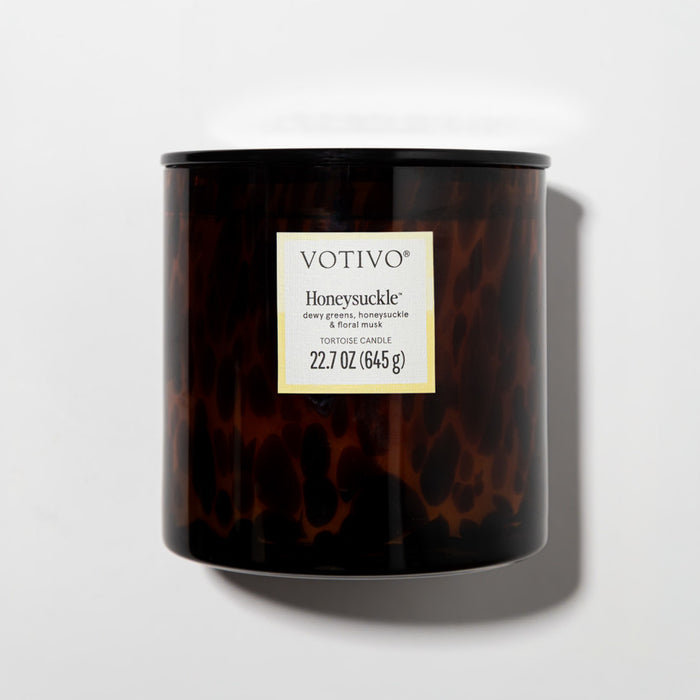 The Votivo Honeysuckle Tortoise Candle, made with a soy blend and weighing 22.7 oz (645 g), showcases dewy greens and floral notes in a brown tortoise-patterned design, pictured on a white background.