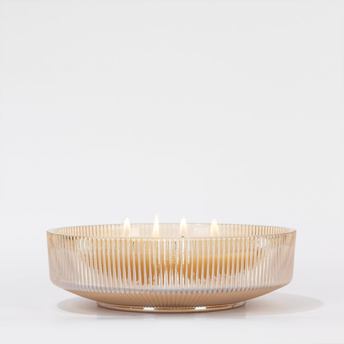 The Votivo Gilded Pear Holiday Multi-Wick Candle, set in a beige ribbed glass bowl with soy blend wax and multiple lit wicks, casts a warm holiday glow against a plain white background.