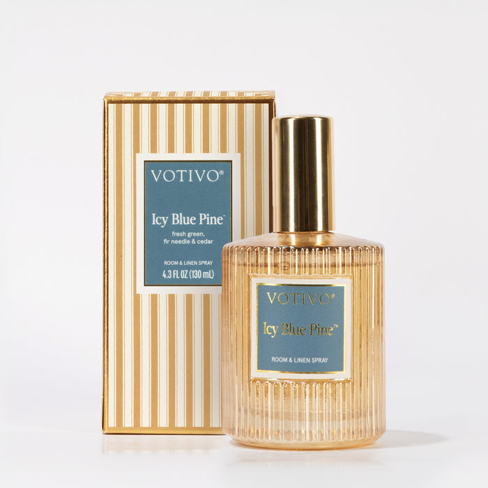 A bottle of Votivo Icy Blue Pine Room & Linen Spray is displayed before its striped box, both showcasing blue labels with gold text. The bottle’s gold cap and ribbed glass add sophistication to this fresh home fragrance.