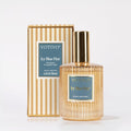A bottle of Votivo Icy Blue Pine Room & Linen Spray is displayed before its striped box, both showcasing blue labels with gold text. The bottle’s gold cap and ribbed glass add sophistication to this fresh home fragrance.