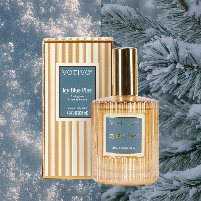 A Votivo Icy Blue Pine Room & Linen Spray stands before its striped box, set against snow-dusted pine and a wintery surface, highlighting this fabric-safe spray’s holiday charm.