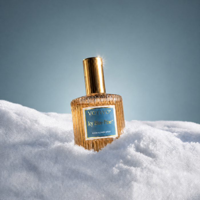 A Votivo Icy Blue Pine room & linen spray bottle sitting in a pile of white fluffy snow