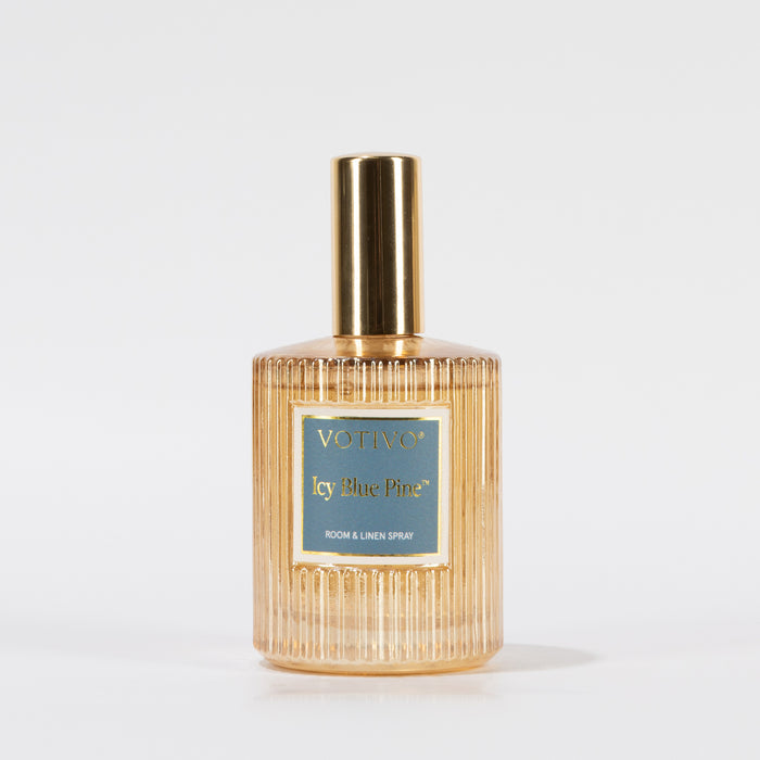 A gold and clear ribbed glass spray bottle labeled Votivo Icy Blue Pine Room & Linen Spray stands upright on a plain white background, ready to infuse your space with a fresh scent.