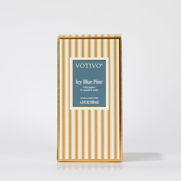 The Votivo Icy Blue Pine Room & Linen Spray features festive fresh green needles and cedar fragrance in a 4.3 FL OZ (130 mL) size, packaged in a rectangular box with vertical gold and white stripes.