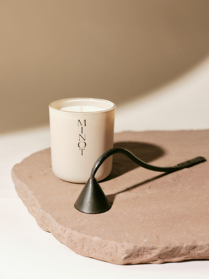 A MINOT candle sits on a stone slab, accompanied by a metal candle snuffer.