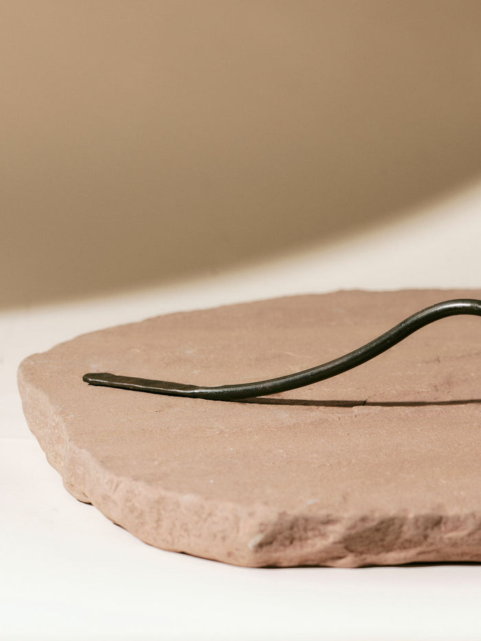 Curved metal handle of a candle snuffer resting on a round, textured stone slab against a neutral background.