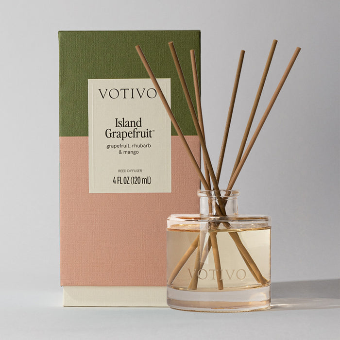 The Votivo Island Grapefruit Reed Diffuser delivers a citrus scent with grapefruit, rhubarb, and mango notes. It comes in a clear glass bottle with wooden reeds and a color-blocked green, pink, and beige box.