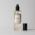 A clear bottle of Votivo Island Grapefruit Room & Linen Spray features a pink and green label, black spray nozzle and cap, all set against a plain light background. Experience the refreshing citrus scent with every spritz.