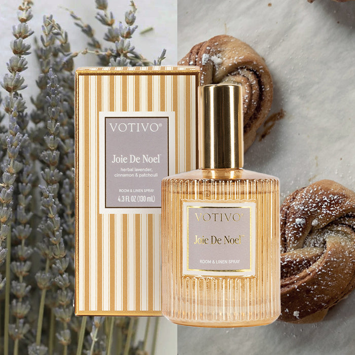A Votivo Joie De Noel Room & Linen Spray bottle with its striped box is shown beside lavender sprigs, while pastries dusted with powdered sugar appear in the background.
