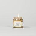 A small Votivo Jungle Bird Discovery Candle burns with a single flame against a white background. This soy blend candle has a white and green label and contains 2.8 oz (80g) of long-lasting fragrance.