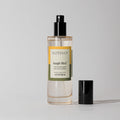 A clear glass bottle of Jungle Bird Room & Linen Spray with a black spray nozzle. The label shows the product name and fragrance description.