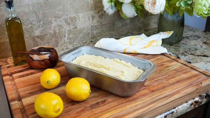 Angled view of Loaf Pan with Tab Handles showing stainless steel finish and batter inside on a wooden cutting board