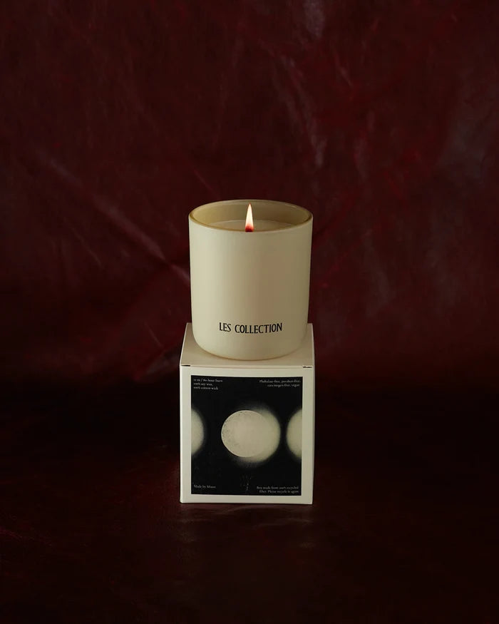 A lit LES Collection Mood candle labeled "Les Collection" sits on a box with a monochrome design, against a dark red background.