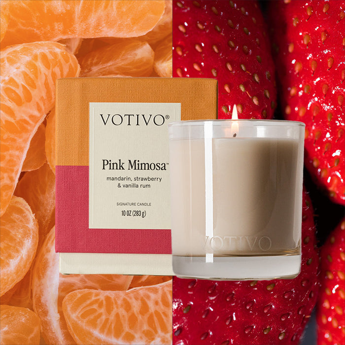 The Votivo Pink Mimosa 10 oz. Signature Candle and its vibrant box are displayed with fresh mandarin segments and strawberries, highlighting the soy blend wax candles scents of mandarin, strawberry, and vanilla rum.