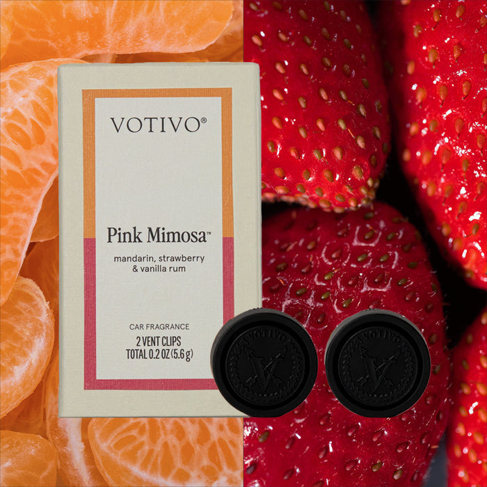 A Votivo Pink Mimosa Car Fragrance (2 Pack) sits beside mandarin and strawberries, suggesting its fruity aroma. Two black Votivo-branded car air freshener clips are placed in front of the box.