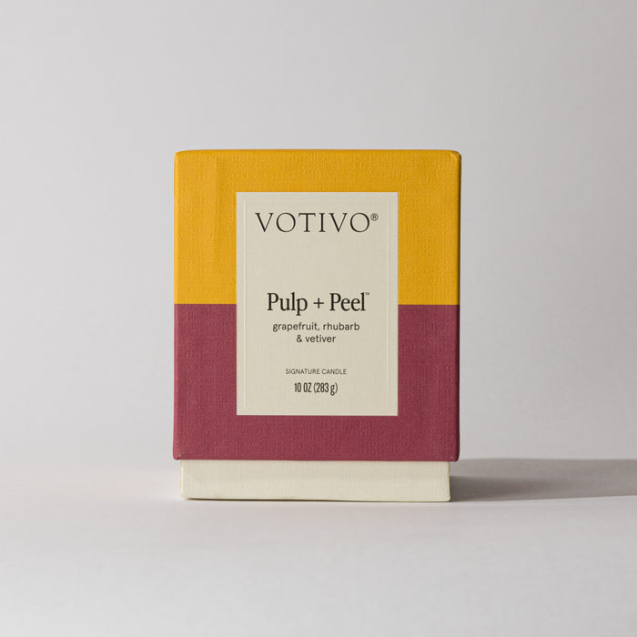 A Votivo Pulp + Peel 10 oz. Signature Candle box, in yellow and maroon blocks, displays its unique grapefruit, rhubarb, and vetiver scent. Made with a soy blend wax (283 g), the candle stands against a plain background.