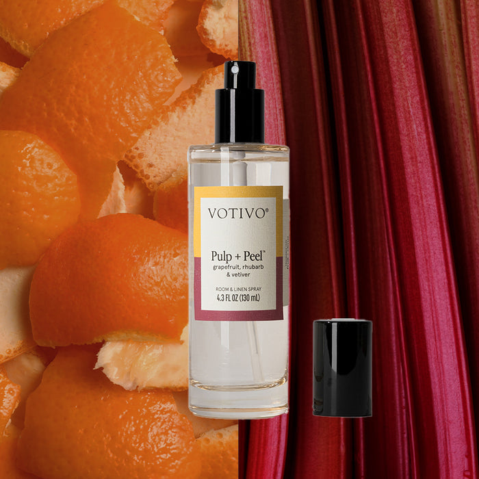 A bottle of Votivo Pulp + Peel Room & Linen Spray, black cap off, is shown with orange peels and red rhubarb. Its label features citrus notes—grapefruit and rhubarb—and confirms its fabric safe.
