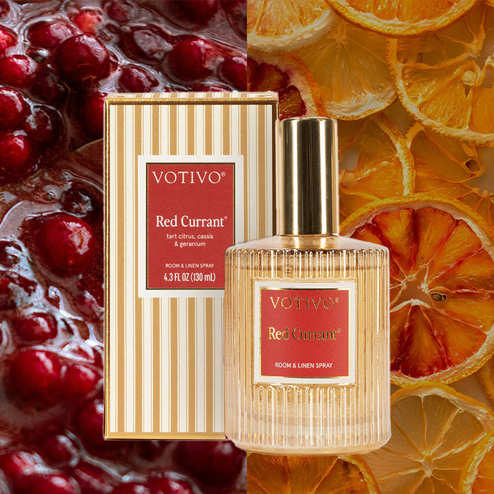 A bottle and box of Votivo Red Currant Holiday Room & Linen Spray are shown against a backdrop of red currants and dried orange slices, emphasizing this fabric-safe spray’s signature red currant scent.