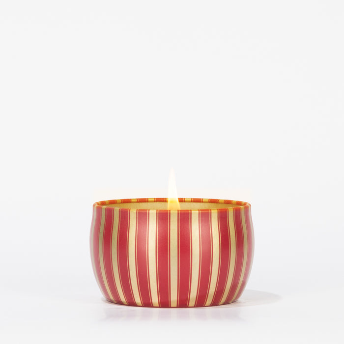 The Votivo Red Currant Holiday Tin Candle features a soy blend wax in a small, round tin with vertical red and gold stripes, displayed against a plain white background.