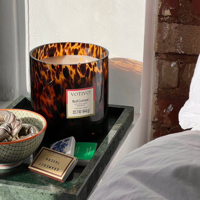 Votive candle in a tortoiseshell glass holder on a nightstand next to a window.