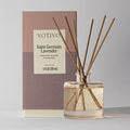 A Votivo Saint Germain Lavender Reed Diffuser with brown reeds in a clear glass bottle sits before its branded packaging featuring product details.