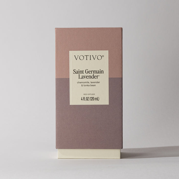 The Votivo Saint Germain Lavender Reed Diffuser comes in a rectangular box with a mauve and taupe design and a centered label listing chamomile, lavender, and tonka bean. This Signature Reed Diffuser delivers an elegant floral scent.