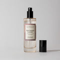 A Votivo Saint Germain Lavender Room & Linen Spray bottle with a black nozzle stands on a plain surface. The cap sits beside it, emphasizing the calming lavender fragrance inside.