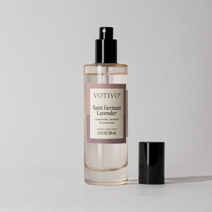 A Votivo Saint Germain Lavender Room & Linen Spray bottle with a black nozzle stands on a plain surface. The cap sits beside it, emphasizing the calming lavender fragrance inside.