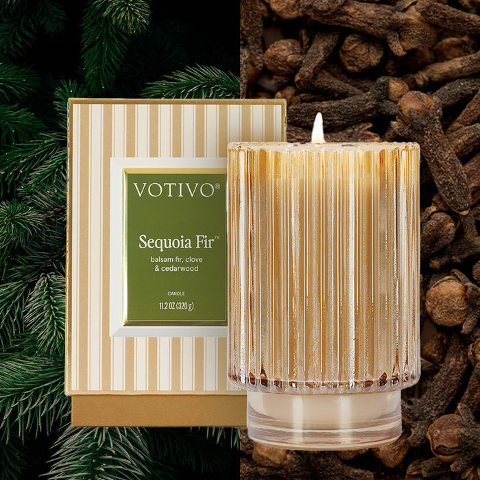 The Sequoia Fir Holiday Candle by Votivo is displayed in a ribbed glass jar with its striped box. Fir branches and cloves set off its balsam fir, clove, and cedarwood scent. Crafted from a soy blend wax for a clean burn.