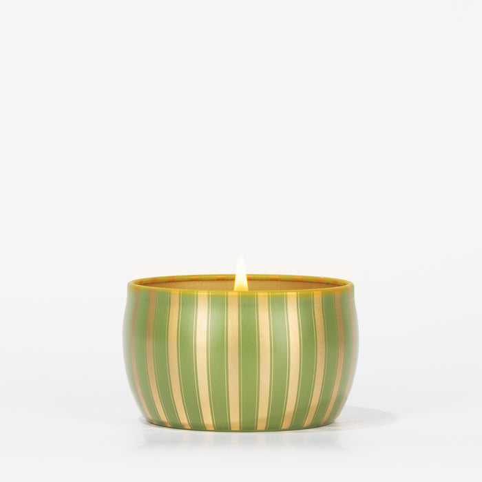 A lit Sequoia Fir Holiday Tin Candle by Votivo sits centered in its round, green and gold Gilded Stripes container against a white background, capturing the cozy holiday charm.