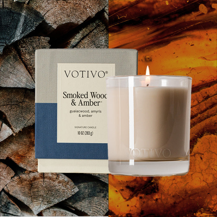 A Votivo Smoked Wood & Amber 10 oz. Signature Candle rests beside its box; behind them, stacked firewood and a close-up of amber resin emphasize the inviting glow of the soy blend wax.