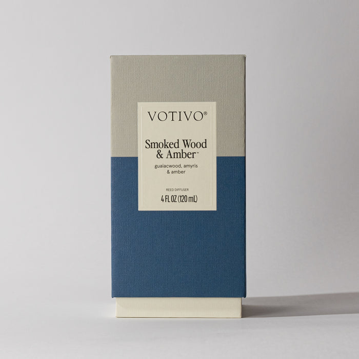 The Votivo Smoked Wood & Amber Reed Diffuser comes in a rectangular, minimalistic beige and blue box, featuring fiber reeds for optimal fragrance diffusion and notes of balsawood, amyris, and amber.