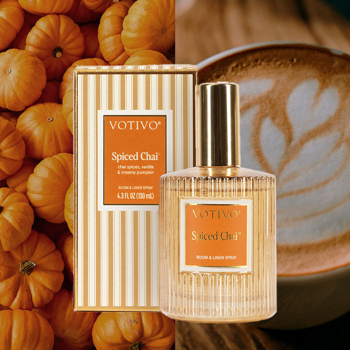 A Votivo Spiced Chai Room & Linen Spray bottle and box, safe for fabric, are displayed with small pumpkins on the left and a latte with heart-shaped foam on the right.
